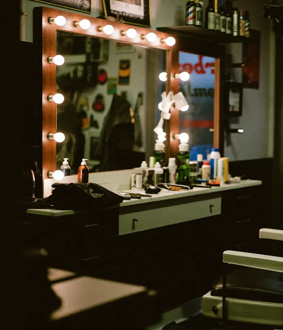 A small barbershop interior at closing time, chair and mirror lit by warm bulbs