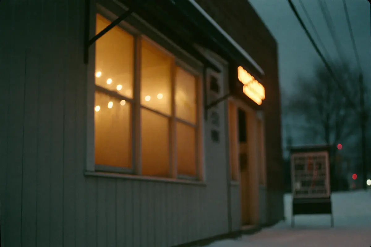 Warm light glowing from a small shop window onto evening snow
