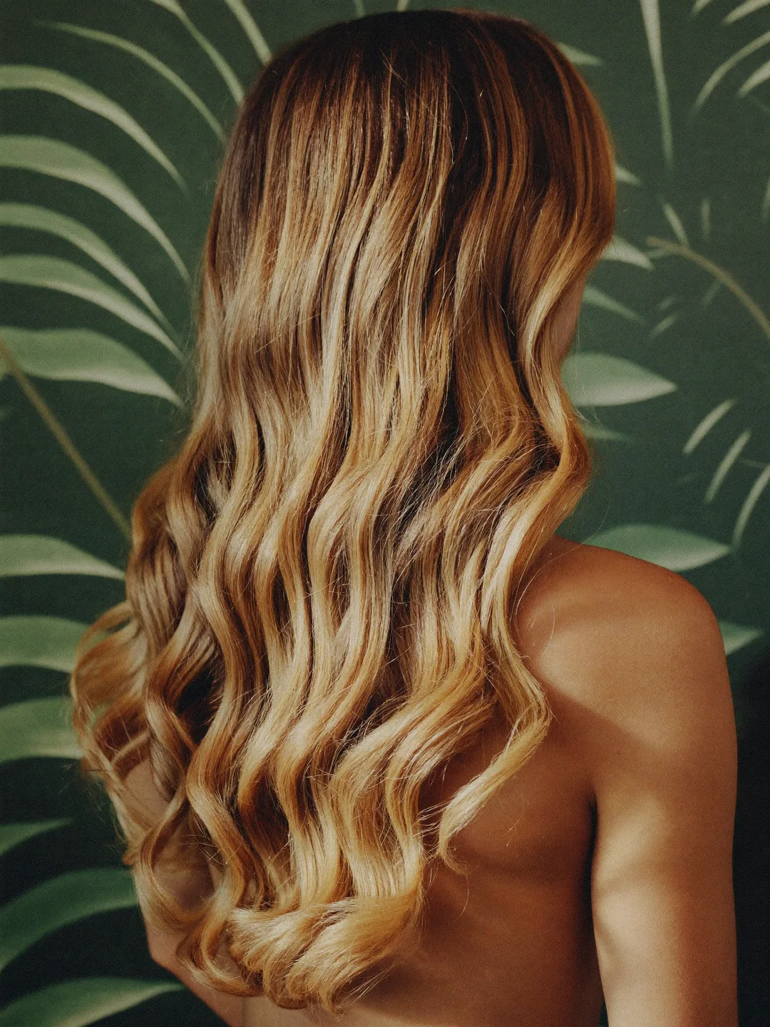 Back view of freshly styled honey-gold balayage waves against botanical wallpaper